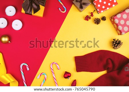 Colorful flatlay with various Christmas items, decor and gifts, including gift boxes, candles, pine cones, candy canes etc. Red and yellow background with copyspace