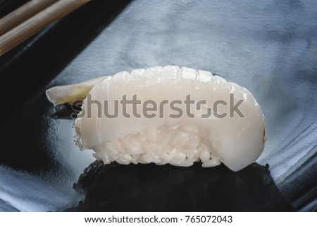 Japanese sushi made of rice and sea bass with chopsticks on a black plate. The horizontal frame.