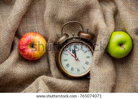 Apples and alarm clock on jute sack background. Autumn season harvest