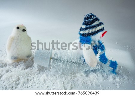 stuffed penguin and  snowman carrying a Christmas tree in snow, against white background