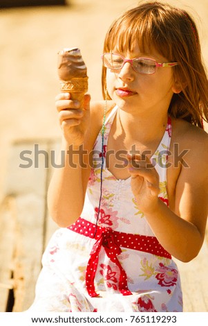 Summertime joy, summer recreation outside concept. Toddler girl in eyeglasses eating ice cream on beach