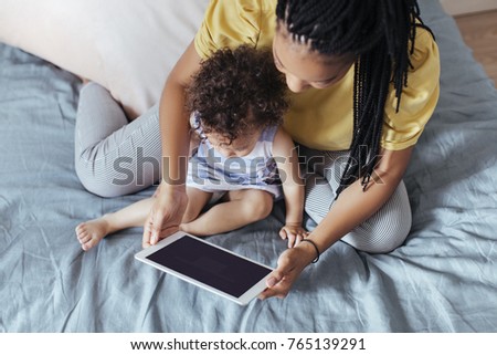 Overhead photo of pretty African woman and her baby daughter looking at tablet.