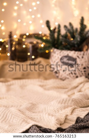 Wicker basket decorated with fir branches and oak wood firewood on the background of a fireplace with garlands. Close-up. Selective focus