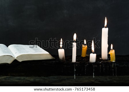 Bible and candle on an old wooden burnt table. Beautiful dark background. Religious concept.