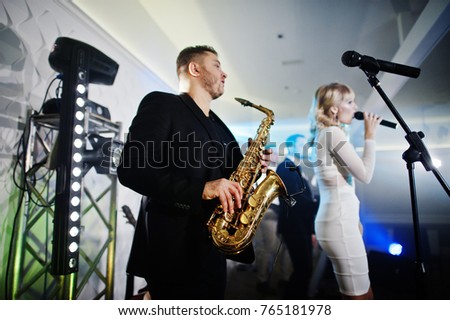 Musicial music live band performing on a stage with different lights. Saxophonist plays.