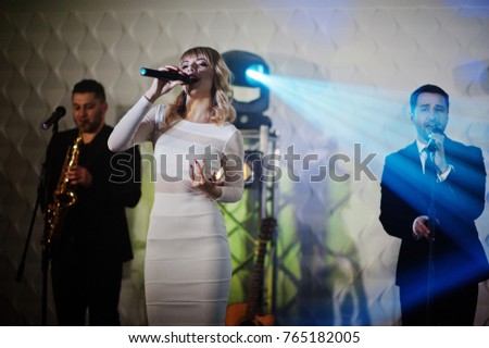 Musicial music live band performing on a stage with different lights. Beautiful blonde vocal singer girl.