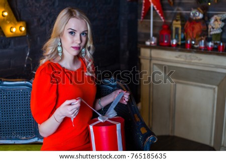 Beautiful young girl in a red dress in a christmas interior with a gift