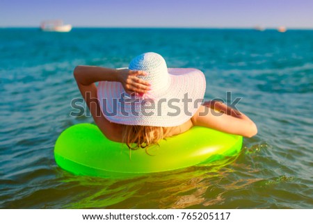Girl in a hat with wide fields floats on a sea wave on a bright green inflatable round mattress rear view.