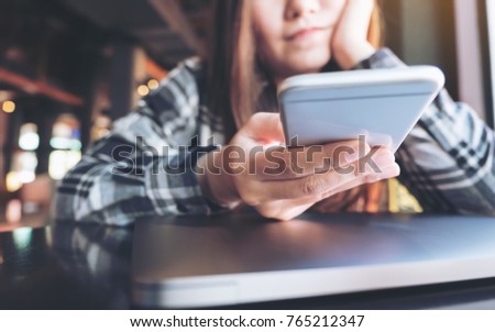 Closeup image of a beautiful Asian woman holding , using and looking at smart phone with feeling relax and laptop on table 