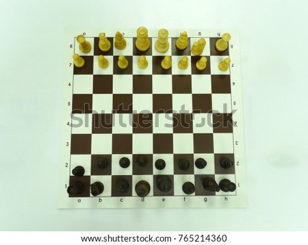 Top view of a chessboard with dark brown and white squares, on which stand figures of dark brown wood and unpainted wood on a light green background