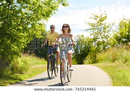 people, leisure and lifestyle concept - happy young couple riding bicycles along road in summer