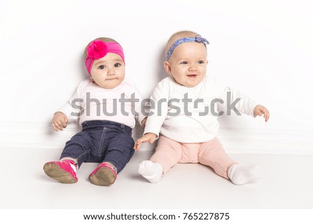 Two babies girls sitting on floor over white wall
