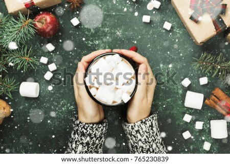 Female hands holding cup with hot chocolate and various attributes of holiday on a green background. Top view