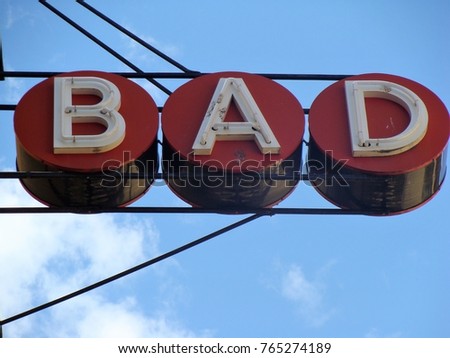 Metal, industrial 'Bad' horizontal sign with sky in background. White letters in red circles surrounded by iron work.