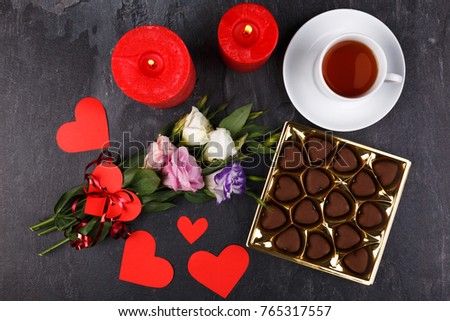 A cup of tea with a box of chocolates and candles on a stone background. View from above