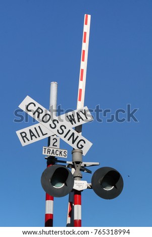 Railway crossing gate sign with light signal and barrier over blue sky background