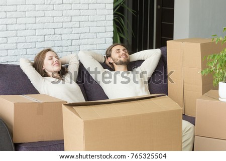 Happy couple relaxing on sofa with boxes, relaxed man and woman resting on couch hands behind head on moving day, dreaming of future in new own home, delivery service for easy move concept Royalty-Free Stock Photo #765325504