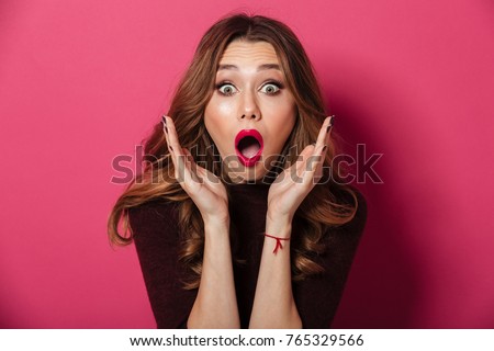 Photo of young surprised beautiful woman standing isolated over pink background. Looking camera.