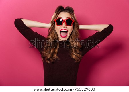 Image of young surprised lady wearing sunglasses standing isolated over pink background. Looking camera.