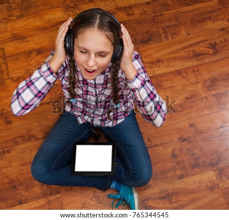 girl in jeans sits on the wooden floor and holding a black tablet pc with blank white screen. Concept of teenage life and gadgets. Top view with copy space.