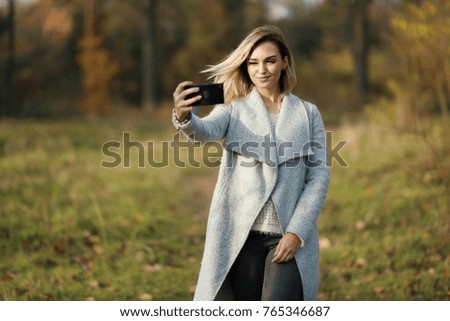 young beautiful girl doing selfie in the park. Autumn background 