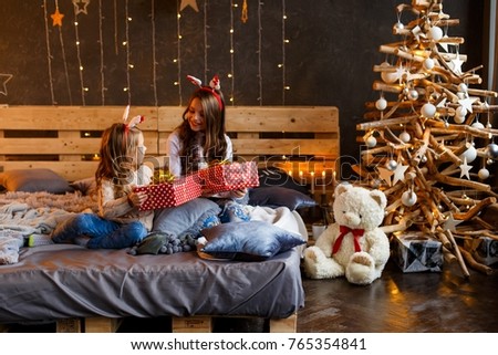 Two beautiful sisters near the christmas tree in front of the fire place having fun. love, family and happiness consept.  New year's eve. Christmas. Cozy holiday at the fir-tree with lights 