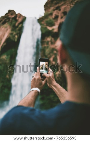 Man taking a cell phone picture of a beautiful blue waterfall