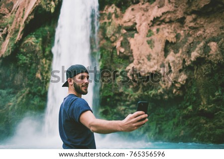 Man taking a cell phone picture of a beautiful blue waterfall