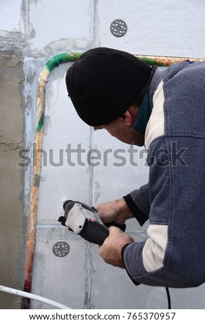 An elderly workman drills a hole in a styrofoam wall for the subsequent installation of a plastic reinforcing dowel. Creating holes in the wall with a drill. Warming of the building facade