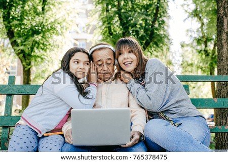 
A father with his daughters sitting on a stone bench, learning to use the laptop. Relaxed autumn day in family outdoors. Lifestyle portrait.


