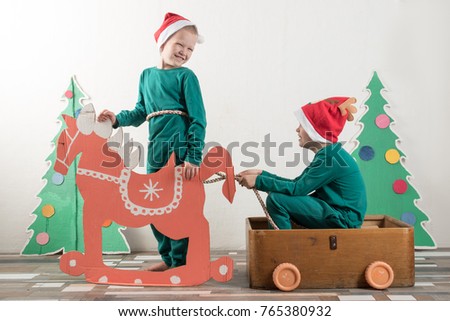 Two funny boys in a Santa Claus hat are playing in a plywood box with cartoon horse. Guys have fun at home. Christmas holiday concept. Copy space.
