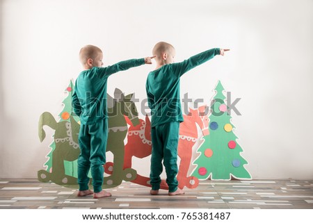 Two funny boys in a Santa Claus hat are playing with horses drawn on cardboard. The guys have fun at home. Christmas holiday concept. Copy space.