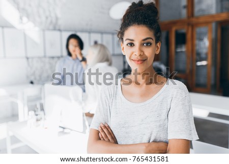 Portrait of inspired female black office worker wearing white t-shirt. Indoor photo of students of international university preparing for exams with charming african girl on foreground.