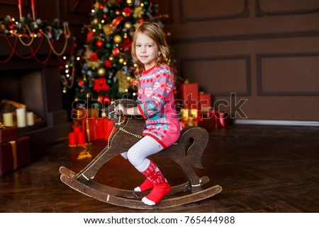 a little cute girl having fun in front of the christmas tree on Christmas eve sitting on the rocking horse. Celebrating New Year