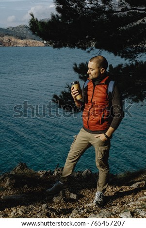 Man traveler wearing a sports vest sits on a mountain with a backpack and thermos in the sea background in Montenegro