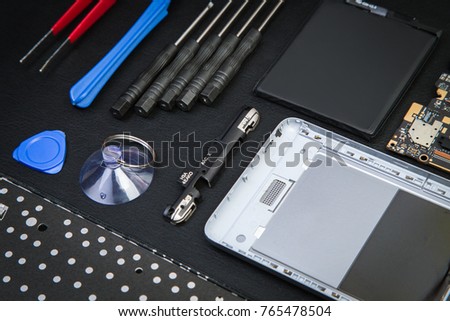 Workplace of the repairman with cell phone and special purpose tools. The disassembled smartphone with tools on a black table
