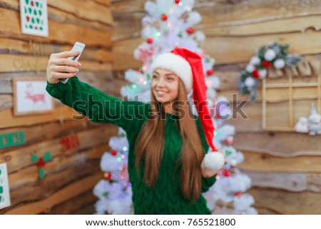 A young girl in a santa hat makes selfie on the background of a Christmas tree