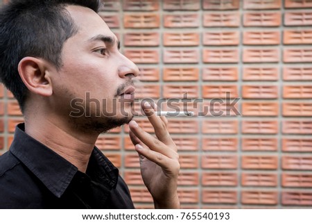 Young asian man smoking cigarette on red brick background and looking to something.Unhealthy lifestyle concept.