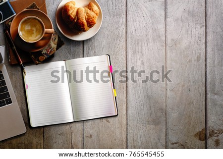 Modern wood office desk table with laptop computer, notebook with  croissant and cup of coffee. Top view with copy space, flat lay.