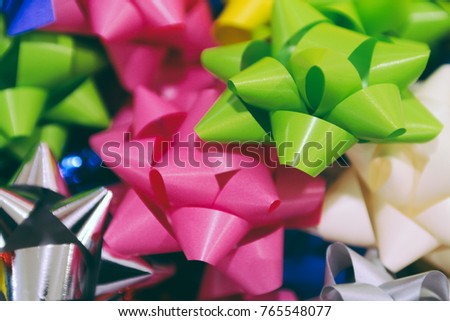 A pile of brightly colored and shiny holiday bows. Many colorful ribbon bows. Package ribbon and materials for holiday gift. Selective focus. Blurred background.