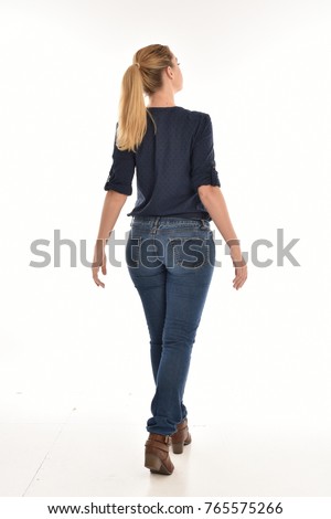 Full length portrait of a girl wearing simple blue shirt and jeans, standing pose facing away on a white background.
 Royalty-Free Stock Photo #765575266