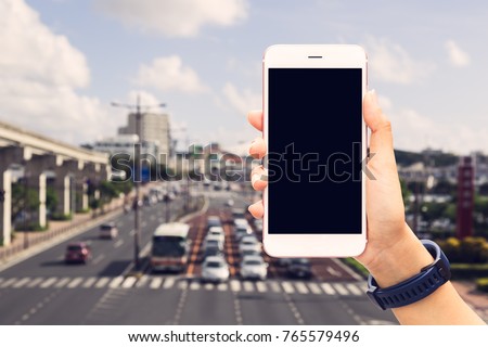Hand holding white mobile smart phone isolated black screen on blur cars waiting the green light signal at intersection