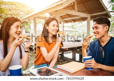 Asian students eating eating the pizza together in breaking time early next study class having fun and enjoy party, Italian food slice with cheese delicious at university outdoor.