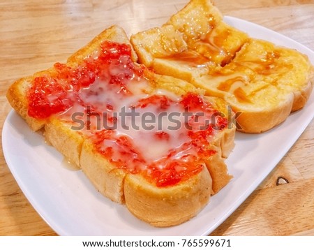 Breads with red jam and yellow butter on white plate and place on wood table. Concept be used for bakery and coffee shop business and billboards. Blur picture.