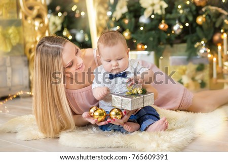 happy family mother and baby little son playing home on Christmas holidays.Toddler with mom in the festively decorated room with Christmas tree. Portrait of mother and baby boy in casual clothes.