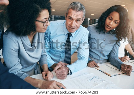 Adult businessman looking at camera while coworing with two African-American women in office.