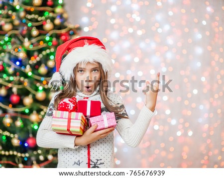 Happy little girl holding many gift boxes and pointing away.Space for text.