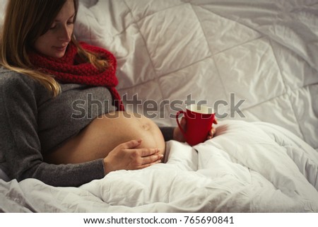 Pregnant young girl in bed looks at the stomach and holds a hand on it.