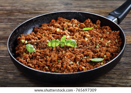 hot juicy ground beef stewed with tomato sauce, spices, basil, finely chopped vegetables and celery in frying pan, classic recipe, side view from above, close-up Royalty-Free Stock Photo #765697309