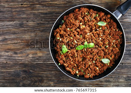 bolognese sauce - hot juicy ground beef stewed with tomato sauce, spices, basil, finely chopped vegetables and celery in skillet on wooden table, authentic recipe, view from above Royalty-Free Stock Photo #765697315